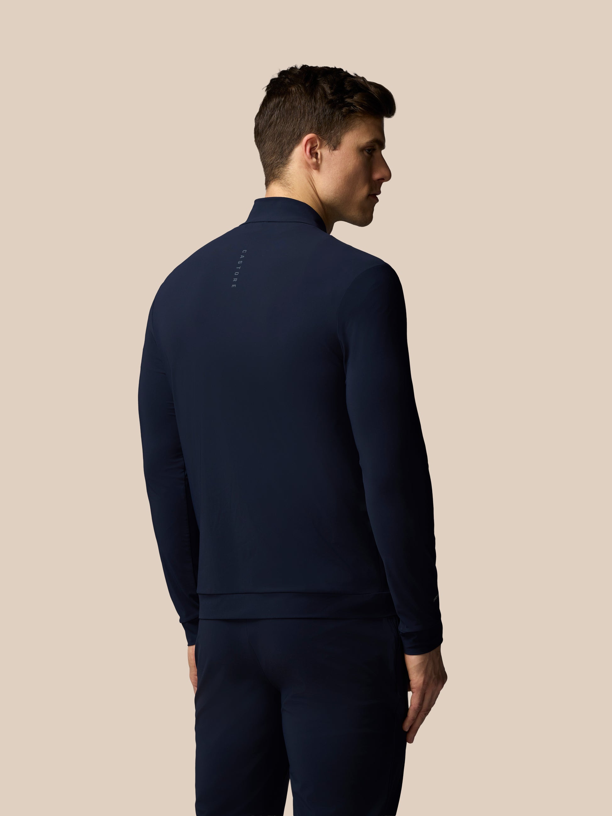 Man wearing a navy blue tracksuit against a beige background