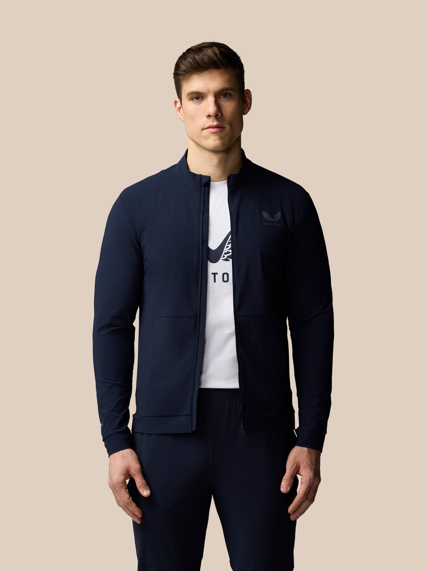 Man wearing a navy jacket over a white t-shirt with a logo on a beige background