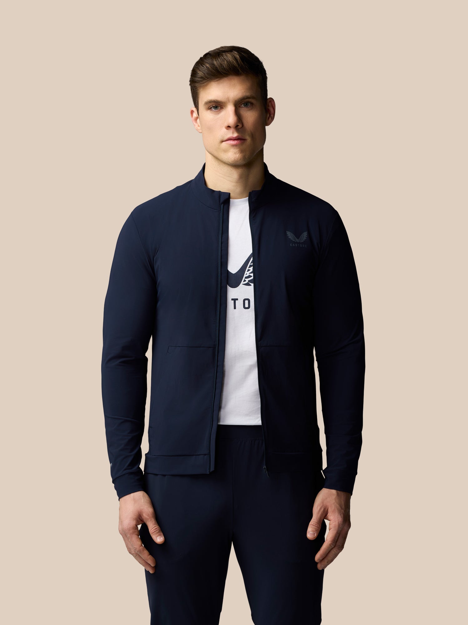 Man wearing a navy jacket over a white t-shirt with a logo on a beige background