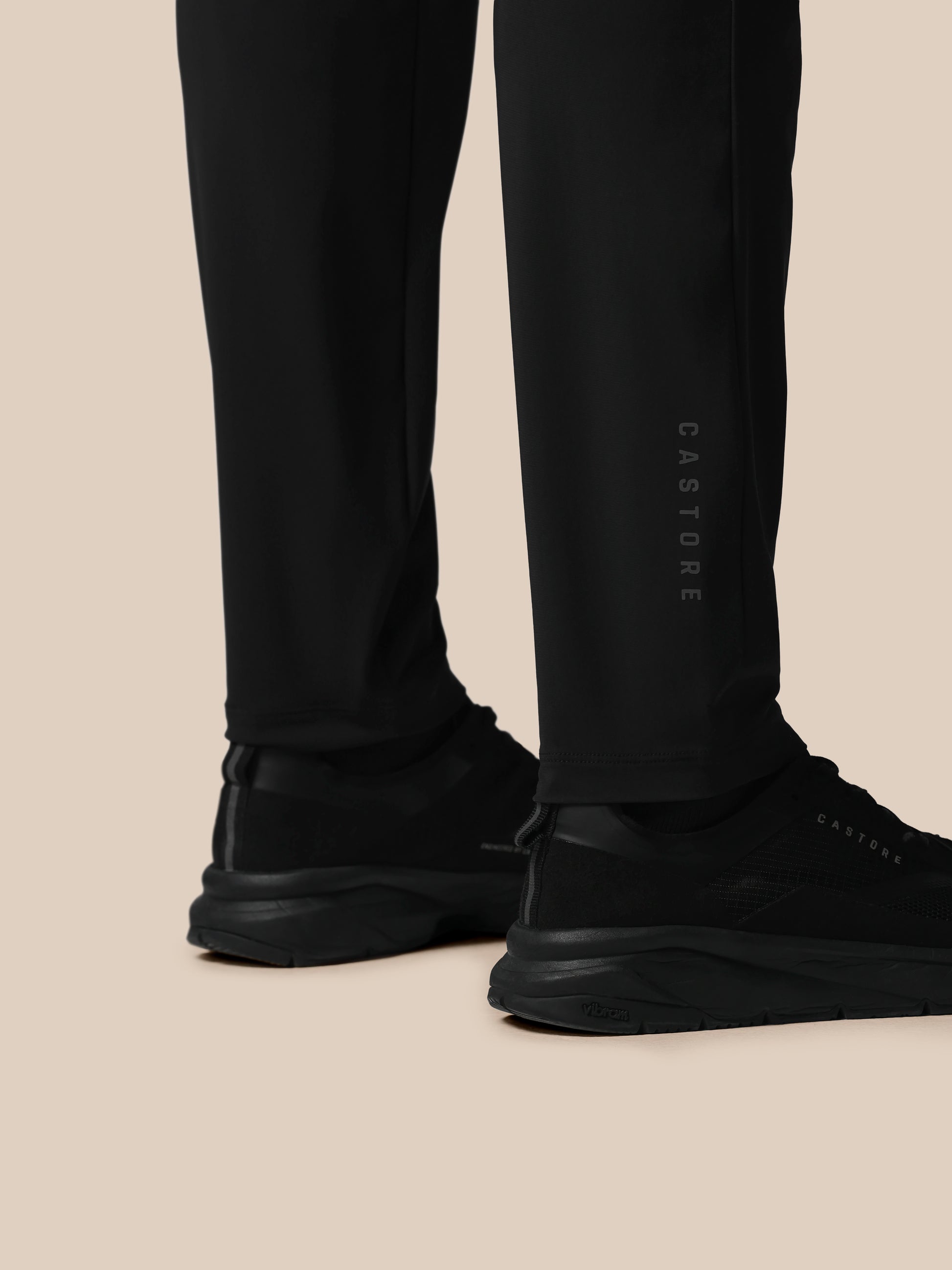 Black pants with 'CASTORE' branding worn by a person on a beige background
