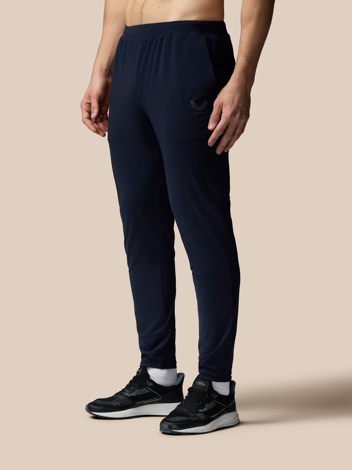 Person wearing navy blue jogger pants and black athletic shoes on a beige background