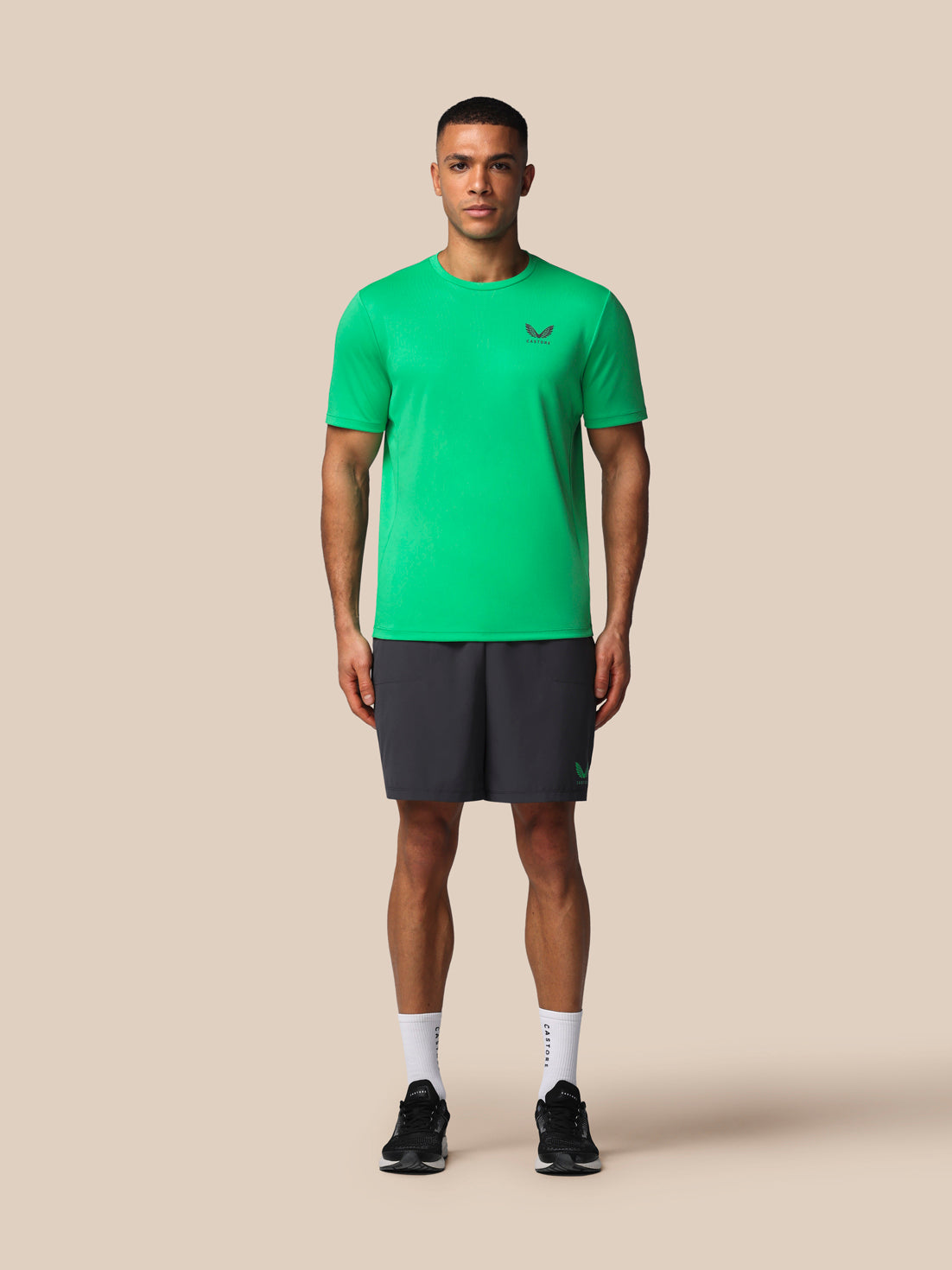 Man wearing a green athletic shirt and black shorts on a beige background