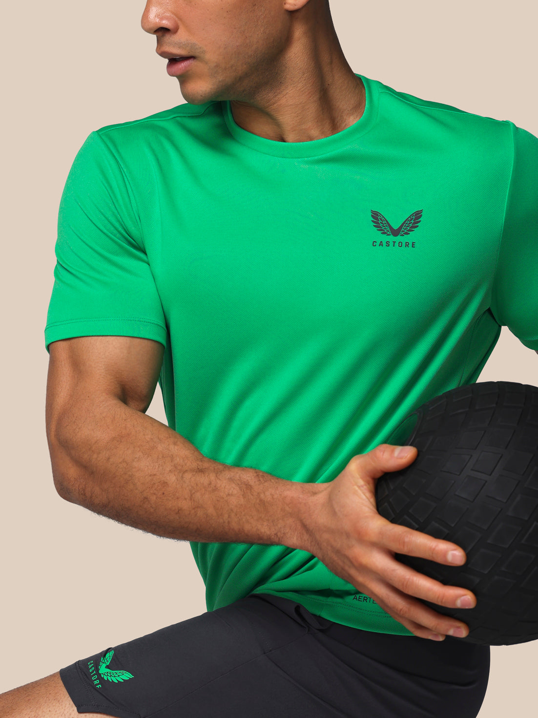 Person wearing a green athletic shirt with a logo, holding a medicine ball.