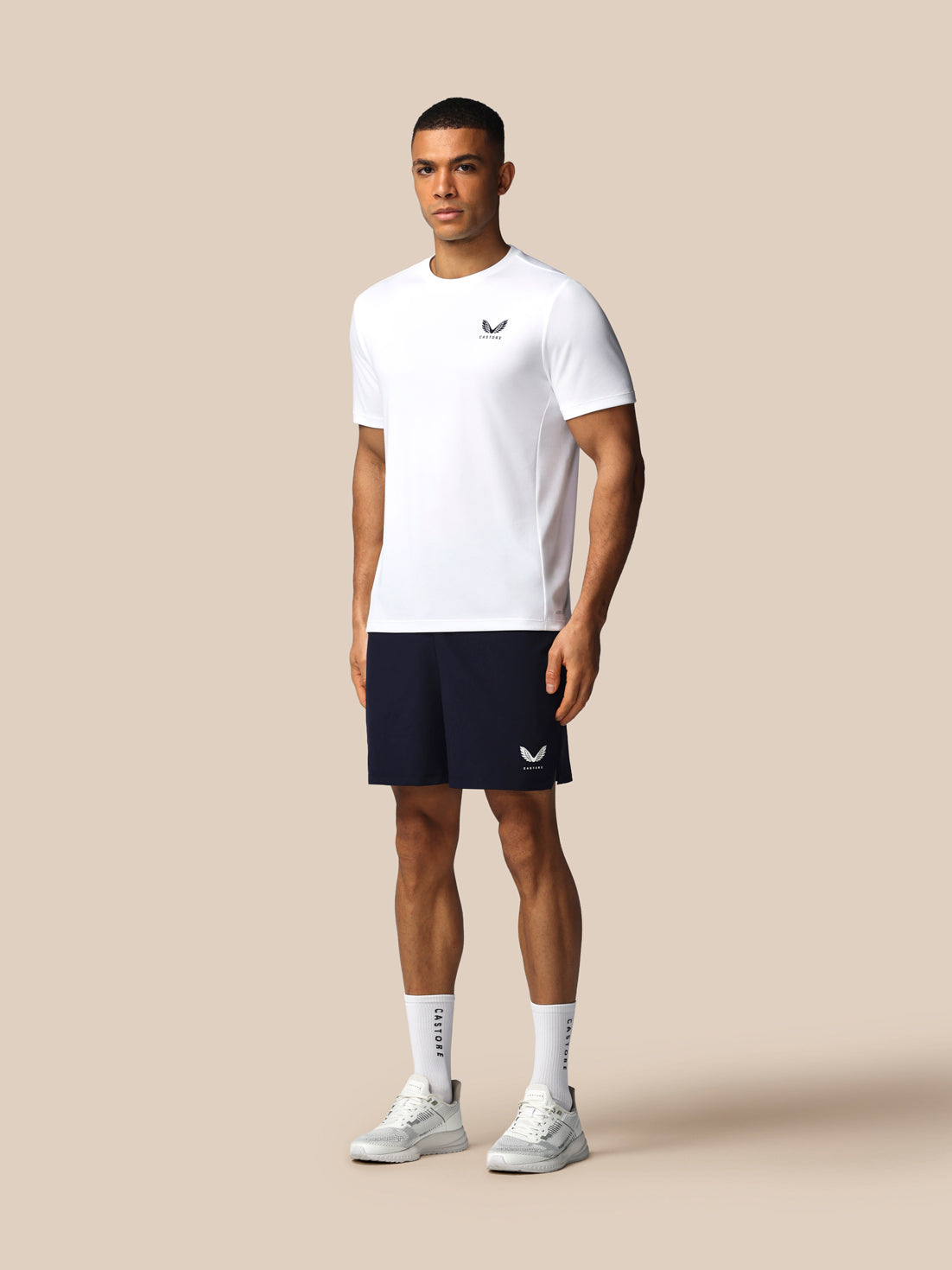 Man wearing a white t-shirt and navy shorts with a logo on a beige background