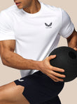 Person wearing a white t-shirt and black shorts with a visible brand logo, holding a black medicine ball.