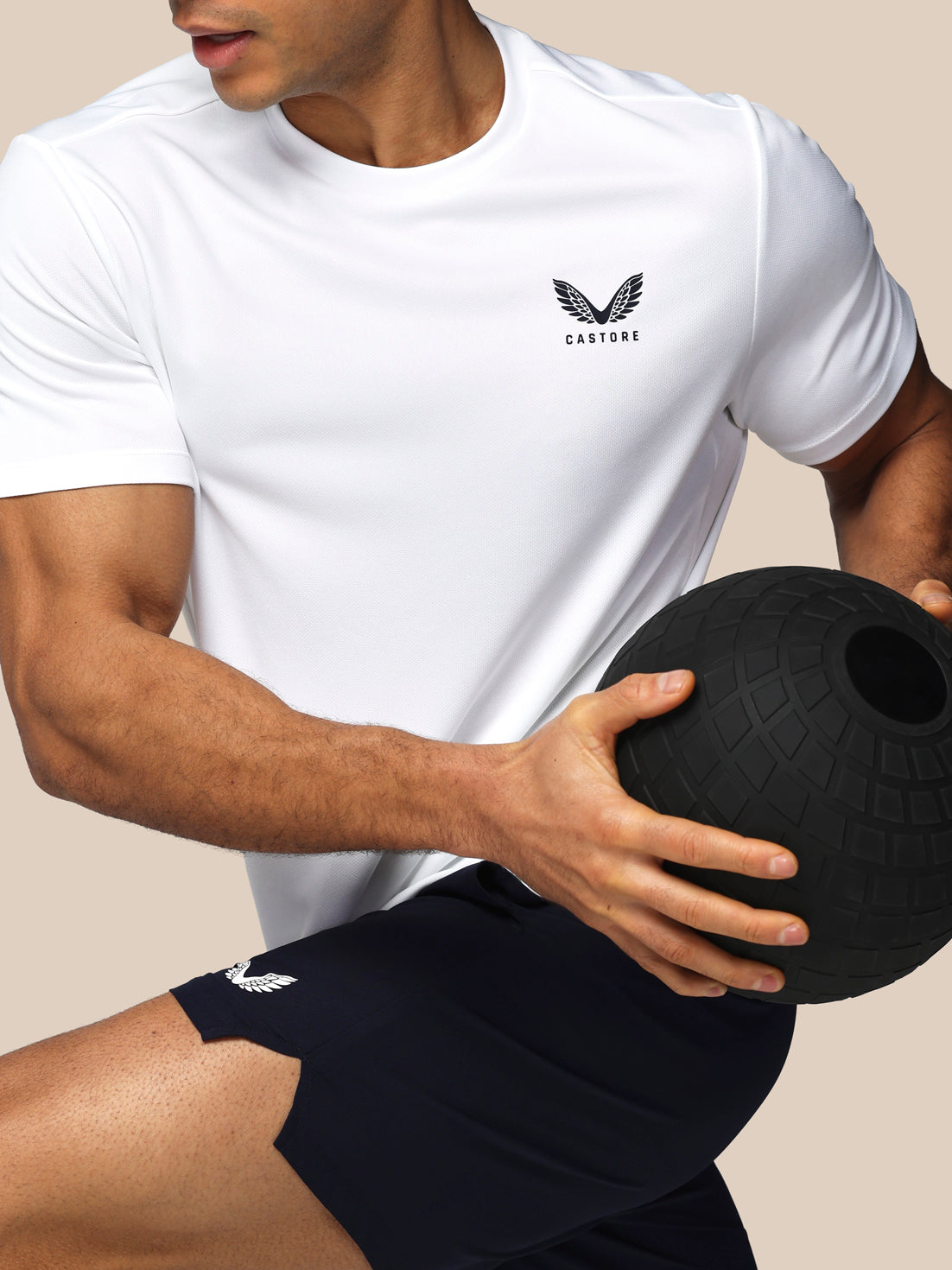 Person wearing a white t-shirt and black shorts with a visible brand logo, holding a black medicine ball.
