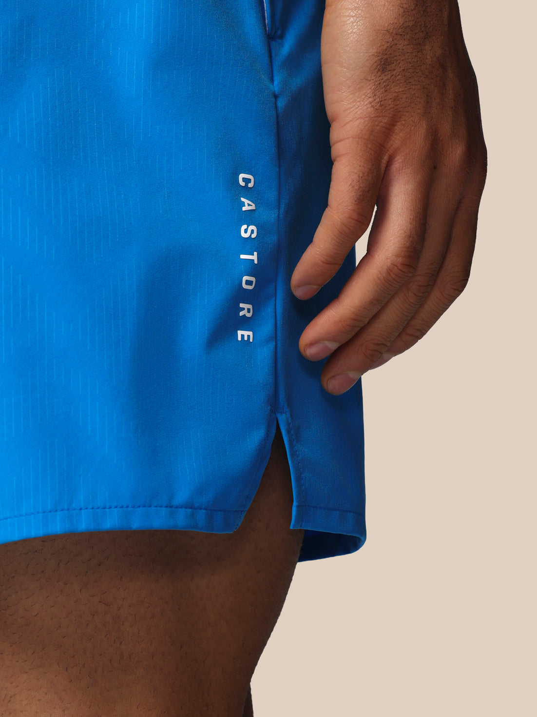 Blue athletic shorts with 'Castore' branding on a beige background