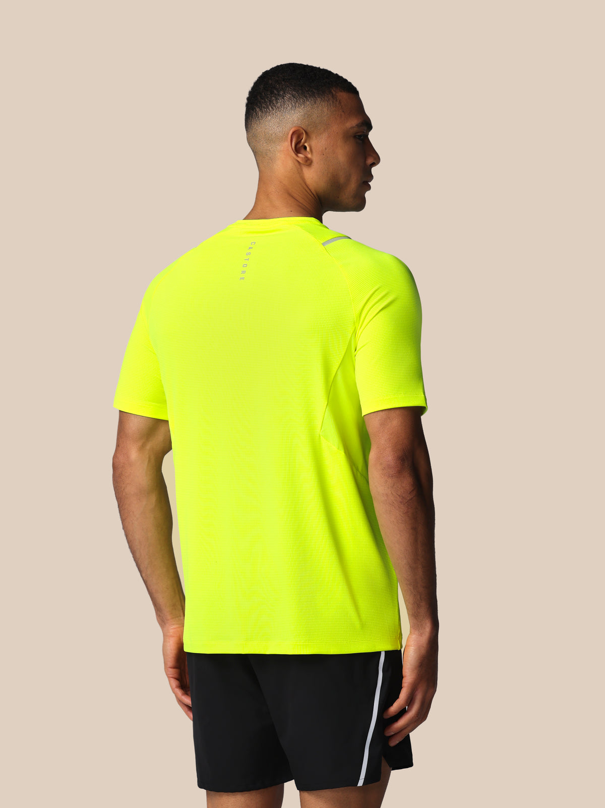 Person wearing a bright yellow athletic shirt and black shorts on a beige background