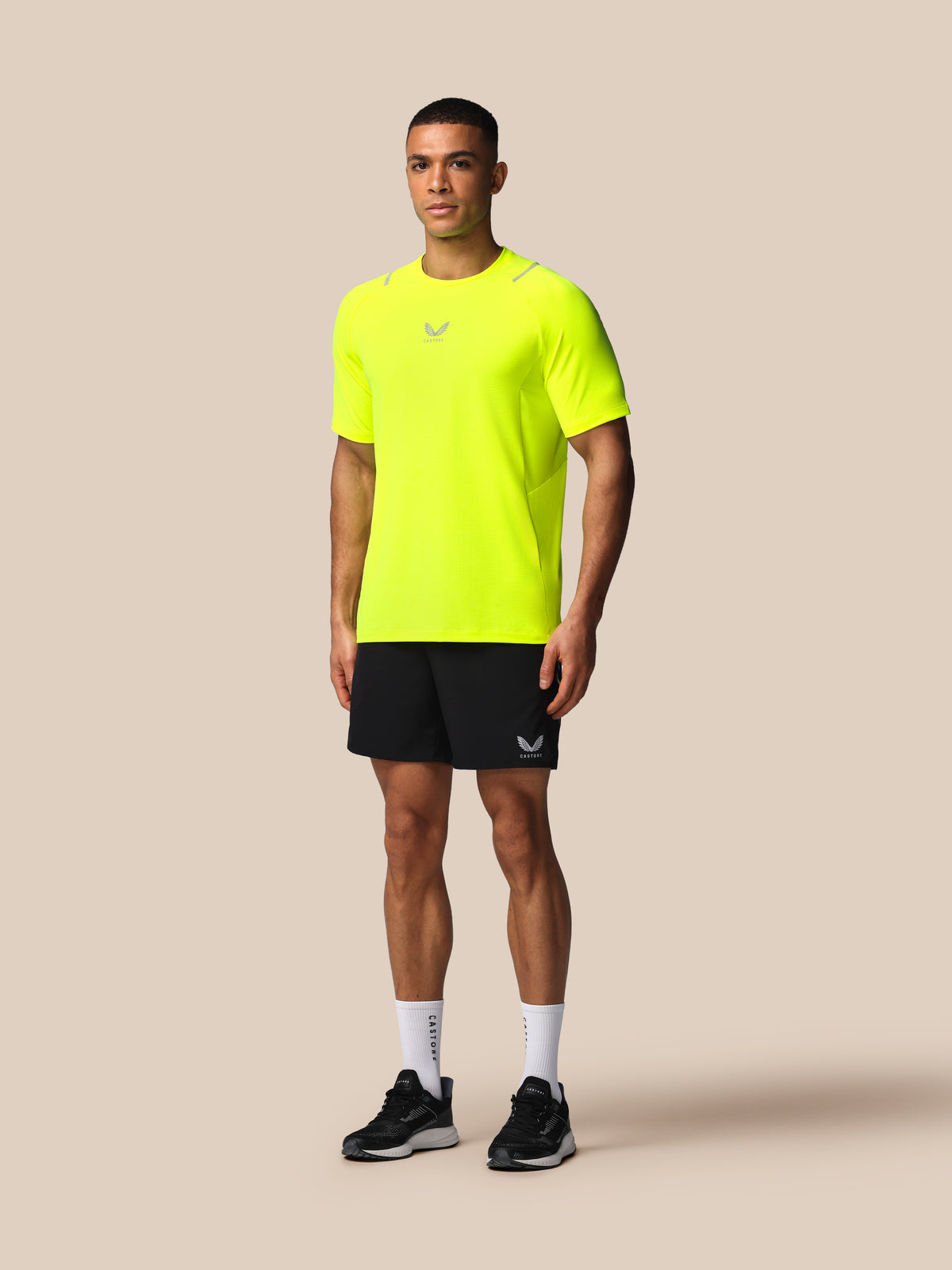 Man wearing a bright yellow athletic shirt and black shorts on a beige background