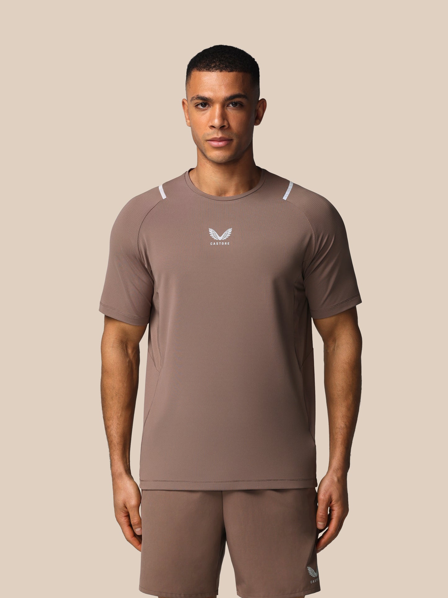 Man wearing a brown athletic outfit with a logo on a beige background