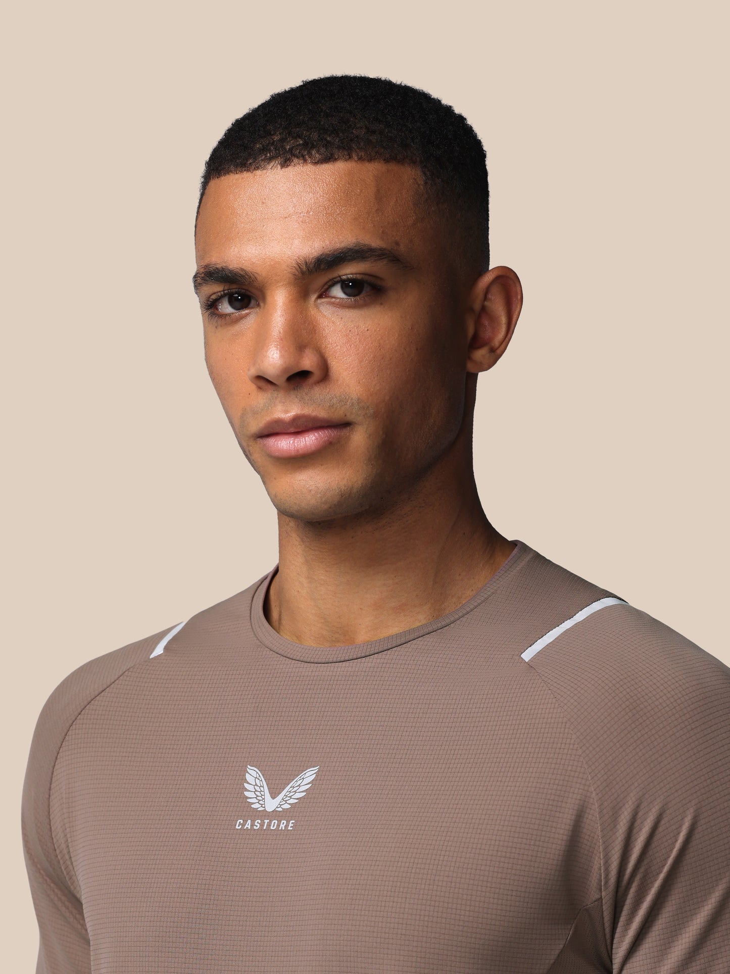 Man wearing a brown athletic shirt with a logo on a beige background