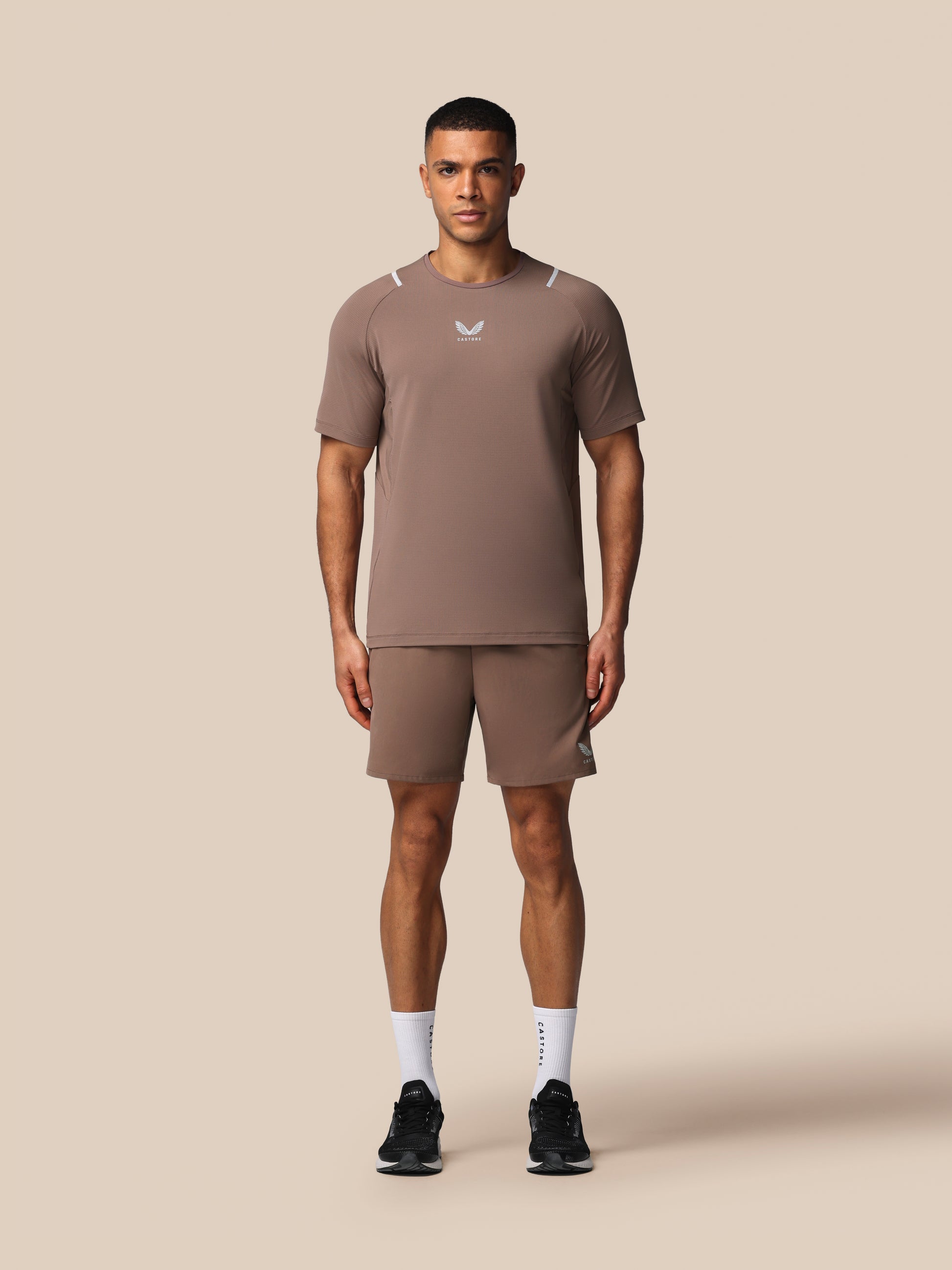 Man wearing a brown athletic outfit with a logo on a beige background