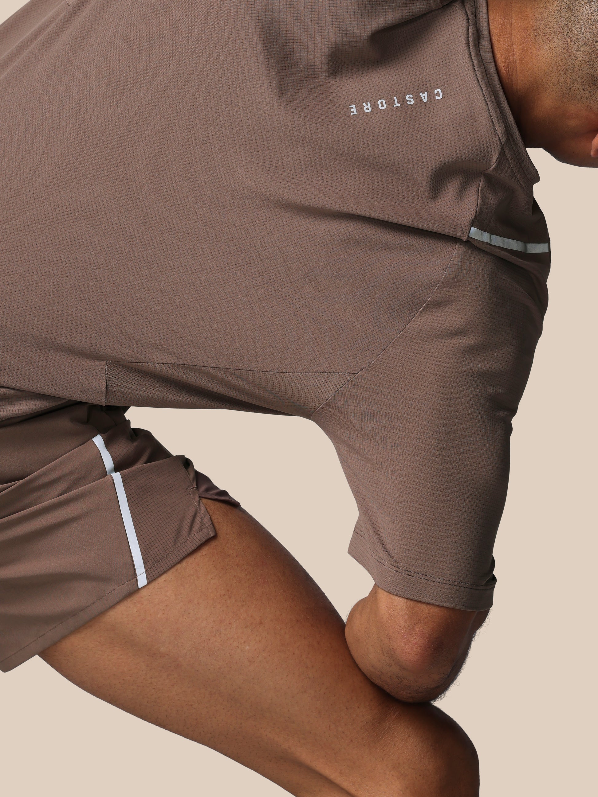 Person wearing brown athletic shorts with 'CASTORE' branding on a beige background