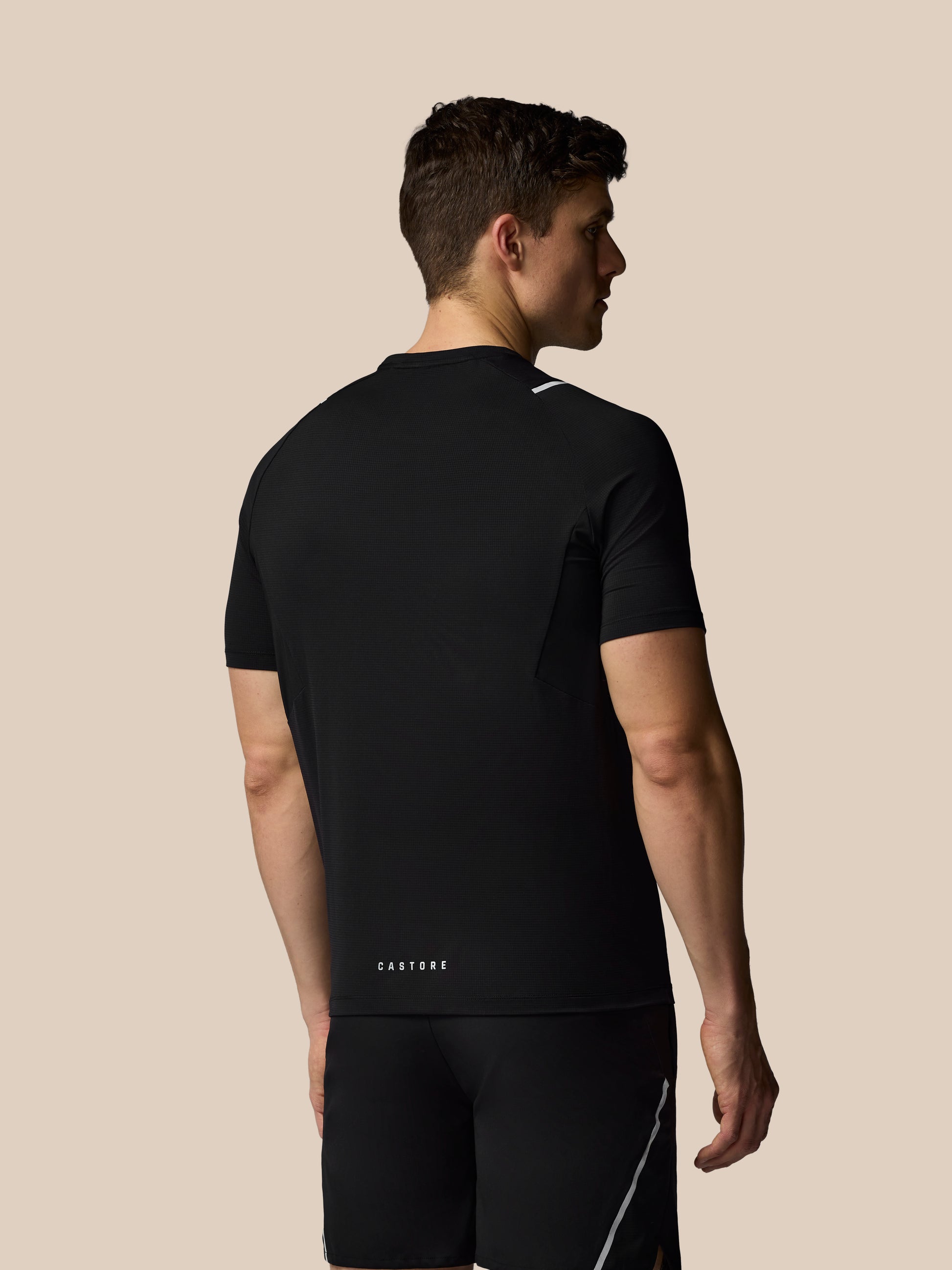 Man wearing a black athletic outfit with 'Castore' branding on a beige background