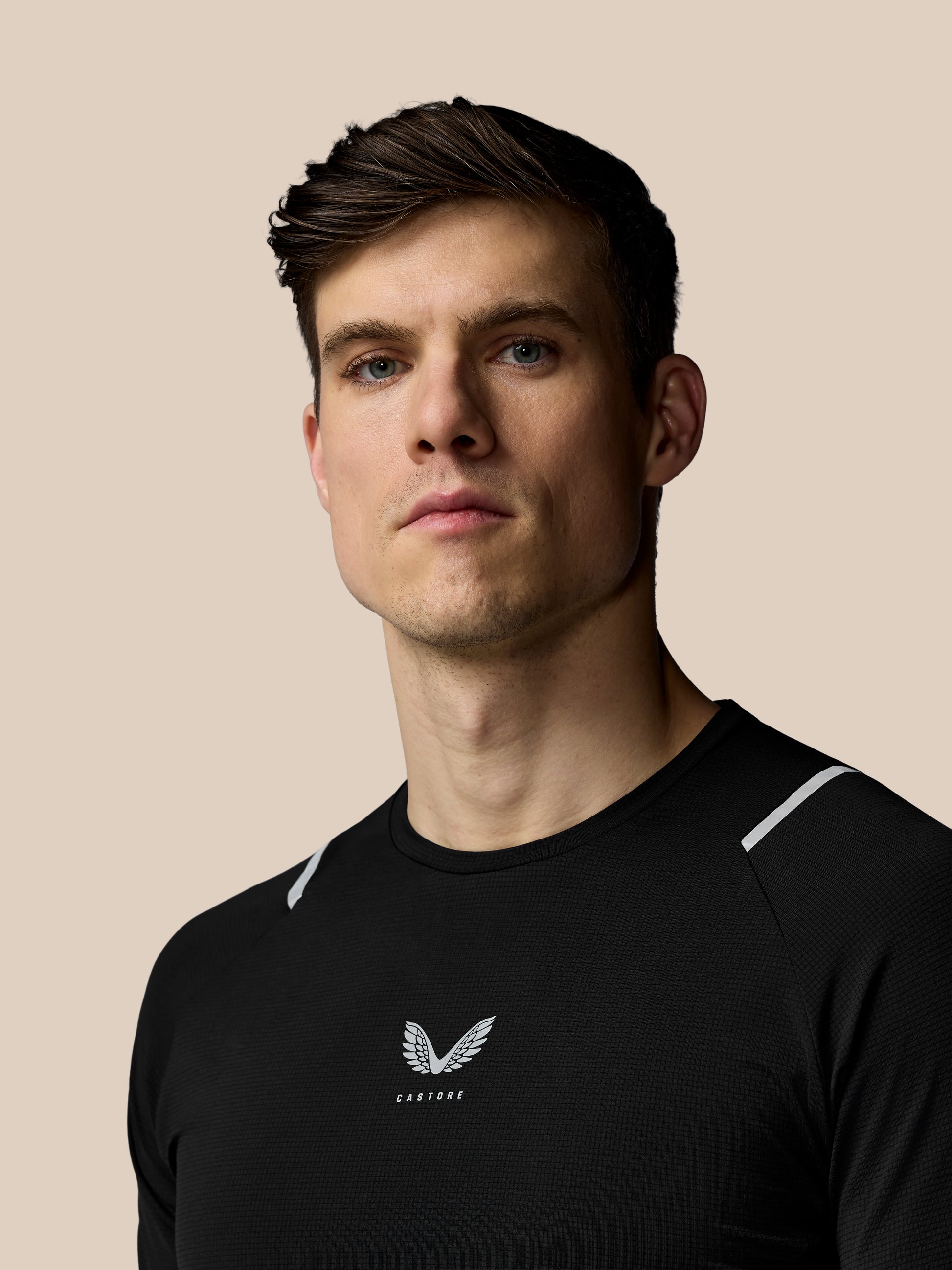 Man wearing a black athletic shirt with a logo on a beige background