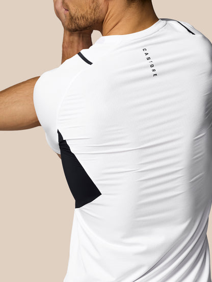 White athletic shirt with black accents and 'Castore' branding on a beige background