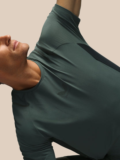 A close-up of a man wearing a dark green athletic short sleeve shirt, shown from the side and back against a solid beige background.
