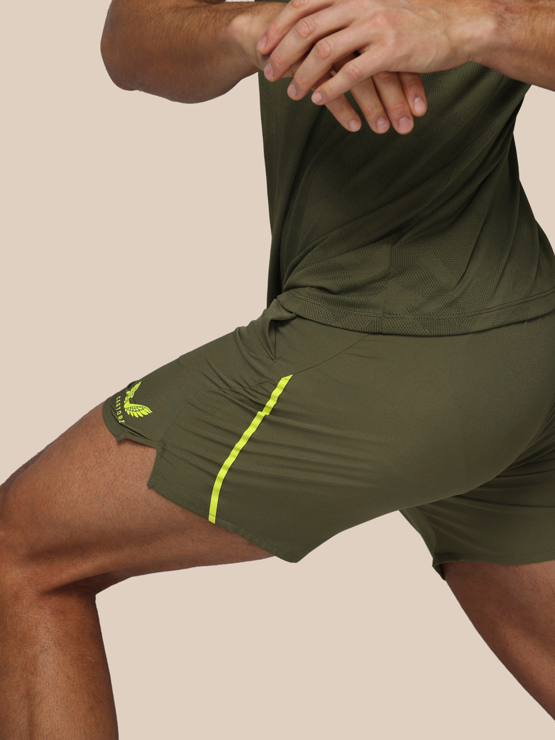 Person wearing green athletic shorts with a yellow stripe on a beige background