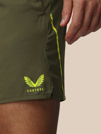 Green athletic shorts with a visible Castore logo on a beige background