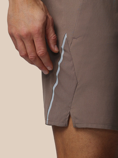 Close-up of a person wearing brown shorts with a white stripe on a beige background