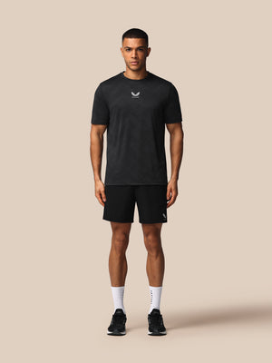 Man wearing a black t-shirt and shorts with a logo on a beige background