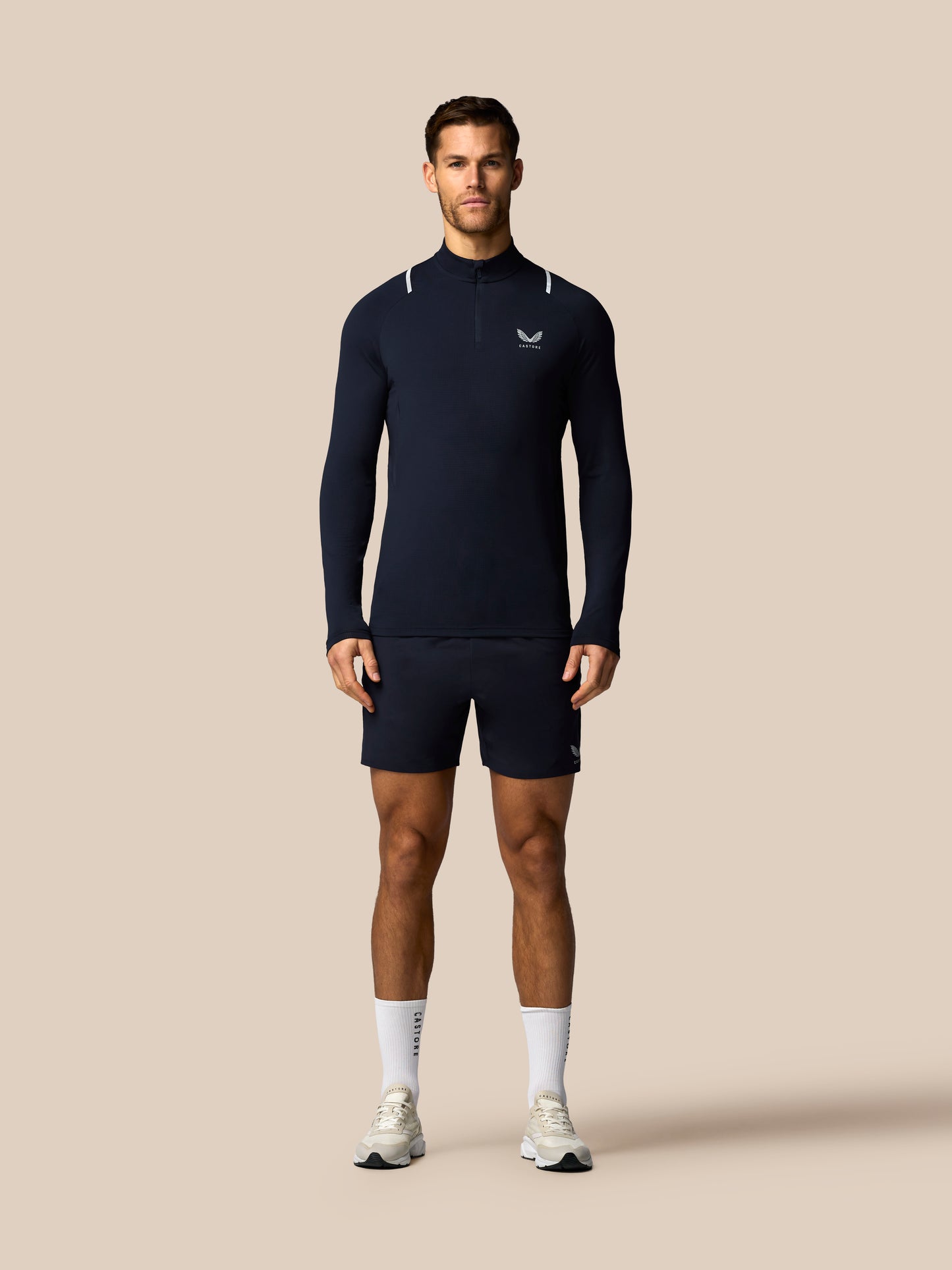 Man wearing a navy long-sleeve athletic shirt and shorts on a beige background