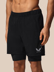 Black athletic shorts with a double-layered design, featuring a white wing logo and the brand name 'CASTORE' on the lower left leg, shown on a model against a solid beige background.