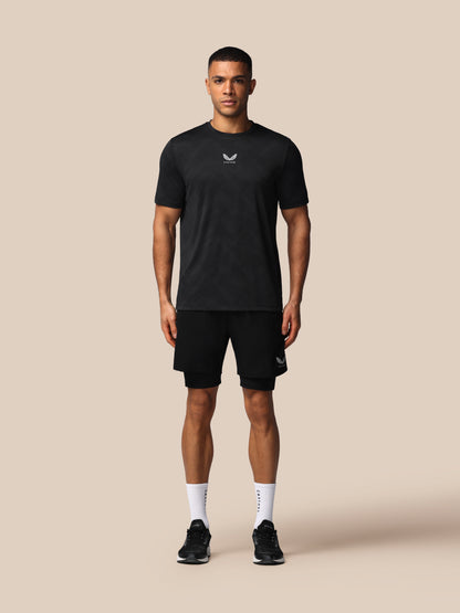 A man modeling a black short-sleeve athletic t-shirt and matching black shorts against a solid beige background.