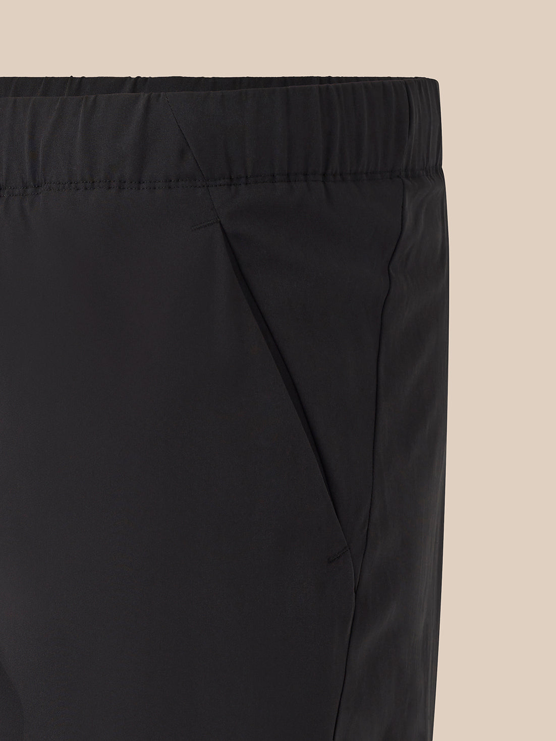 Close-up of black elastic-waist pants showing the waistband and side seam against a light beige background.