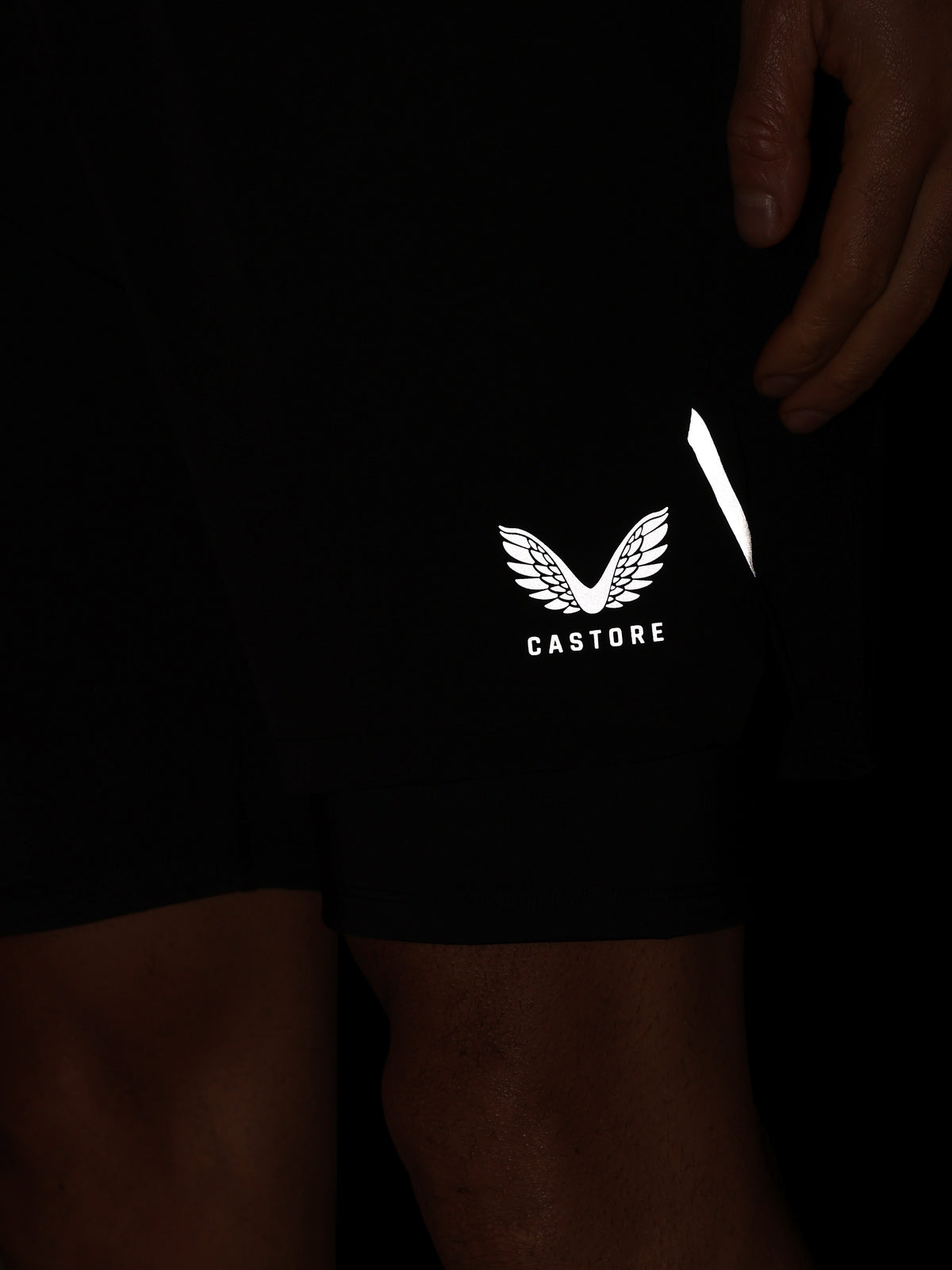 Close-up of black athletic shorts worn by a person, featuring a white Castore wing logo and a reflective white strip on the side.
