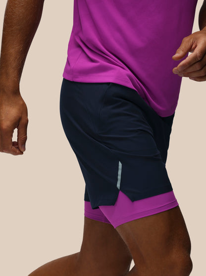 A close-up of a person wearing dark navy athletic shorts with a bright purple inner layer and a matching purple top, shown against a plain beige background.