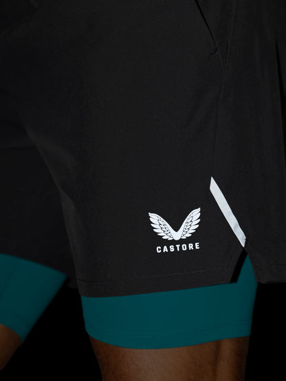 Close-up of black athletic shorts with a white Castore wing logo and a white reflective stripe, worn over teal compression leggings.
