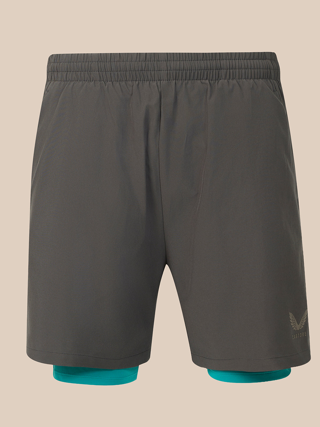 Dark gray athletic shorts with an elastic waistband, featuring a small tonal logo on the lower left leg and teal inner liner cuffs visible at the hem, shown against a solid beige background.
