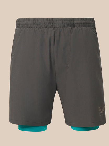 Dark gray athletic shorts with an elastic waistband, featuring a small tonal logo on the lower left leg and teal inner liner cuffs visible at the hem, shown against a solid beige background.