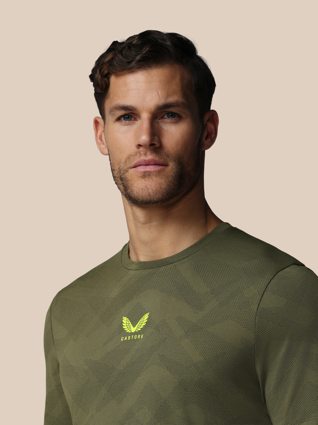 Man wearing a green athletic shirt with a logo on a beige background