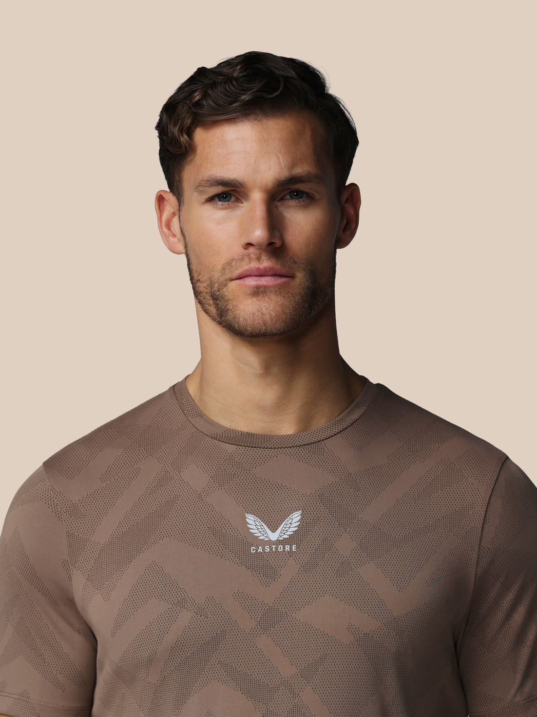 Man wearing a brown athletic shirt with a logo on a beige background