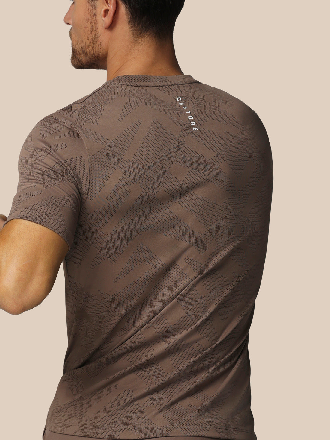 Man wearing a brown t-shirt with a logo on the back against a beige background