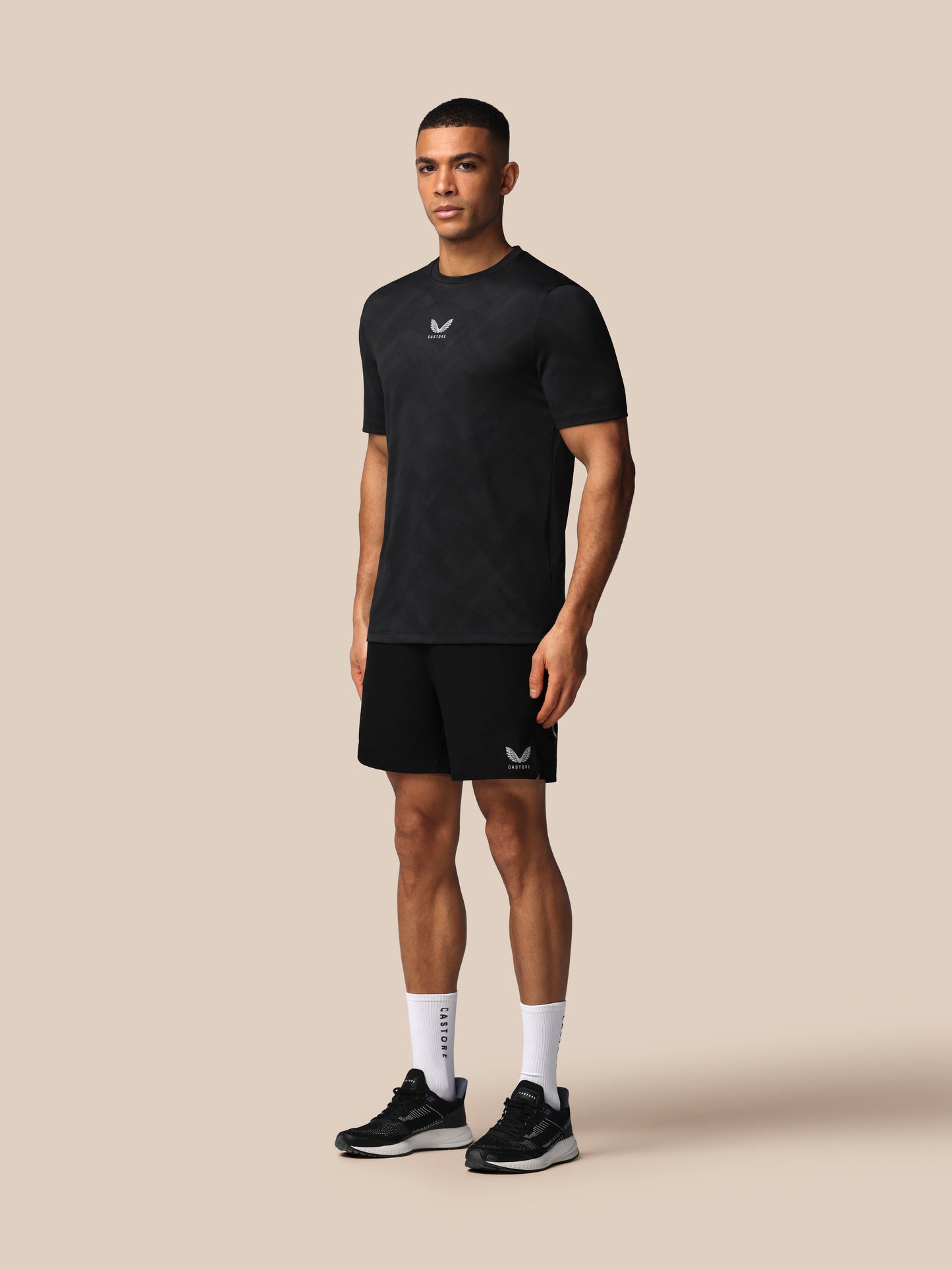 Man wearing a black t-shirt and shorts with a logo on a beige background