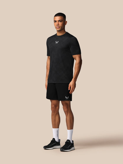 Man wearing a black t-shirt and shorts with a logo on a beige background