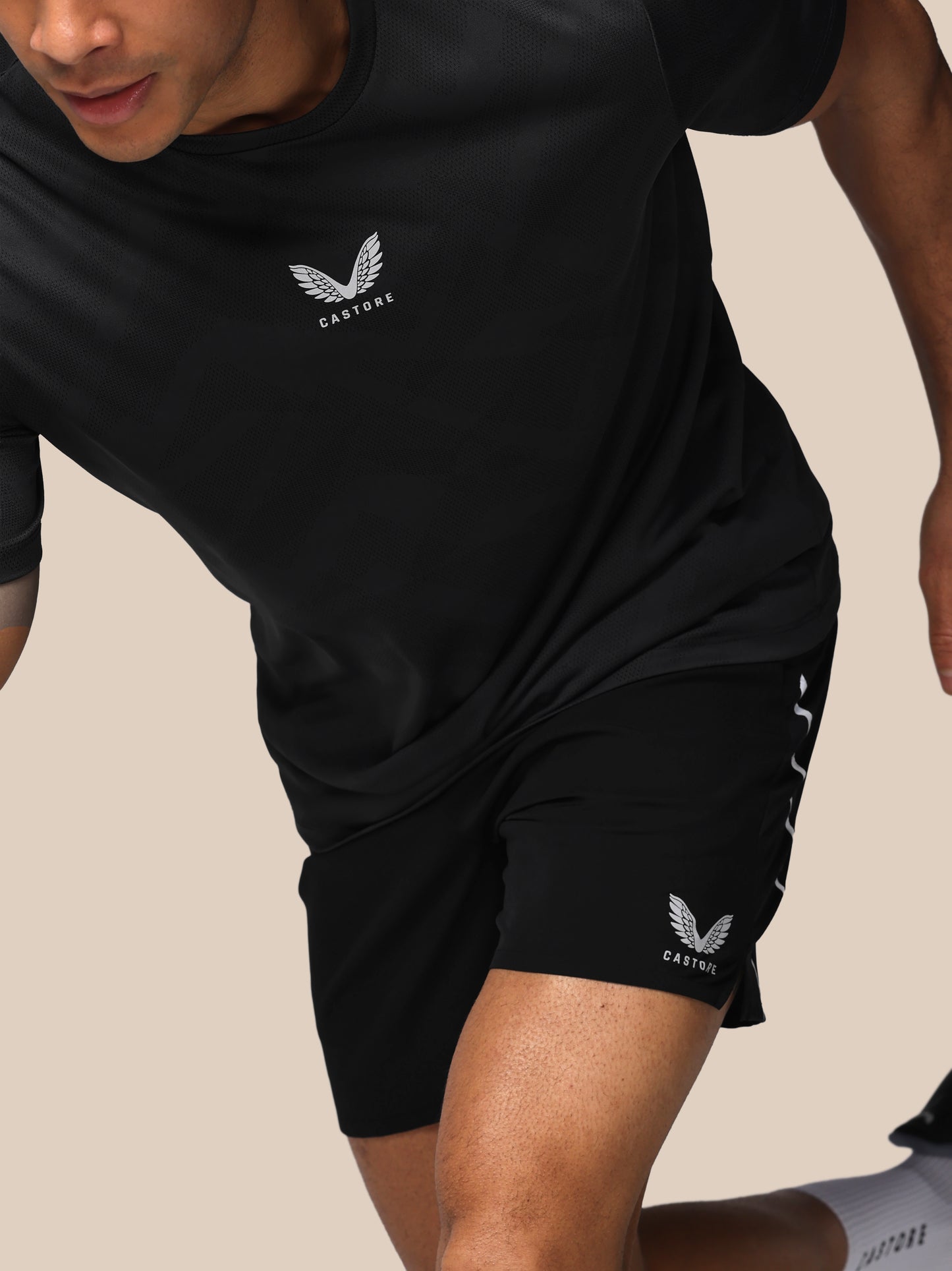 Person wearing black athletic shorts and shirt with a logo on a beige background