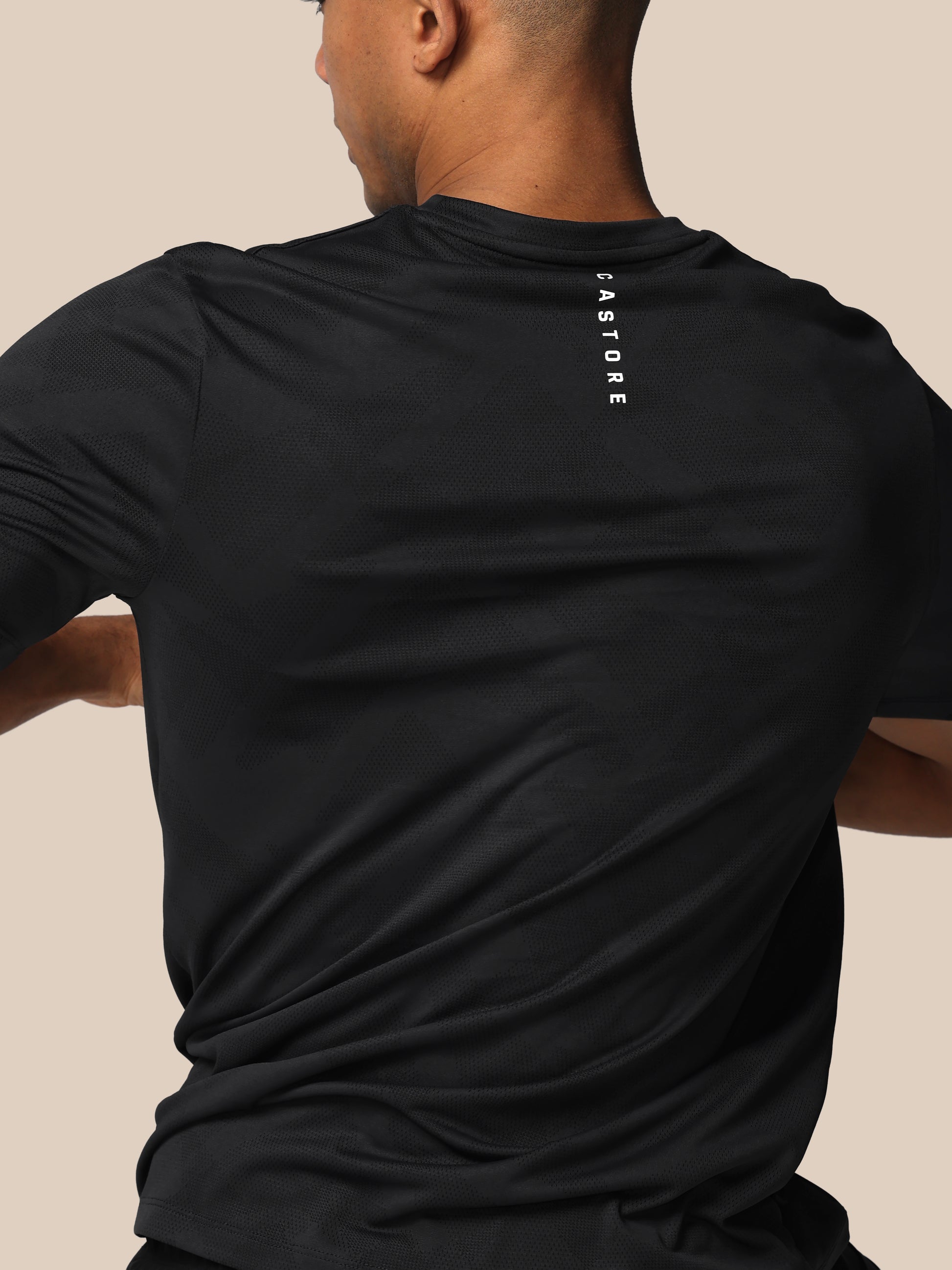 Person wearing a black t-shirt with 'Castore' branding on the back against a beige background