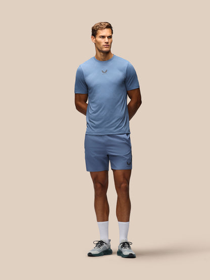 A man modeling a light blue athletic t-shirt and matching shorts against a solid beige background.