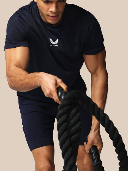 Person exercising with battle ropes wearing a black t-shirt with a logo on a beige background