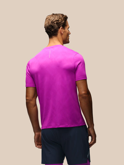 A man shown from the back wearing a bright magenta athletic t-shirt and navy blue shorts against a solid beige background.