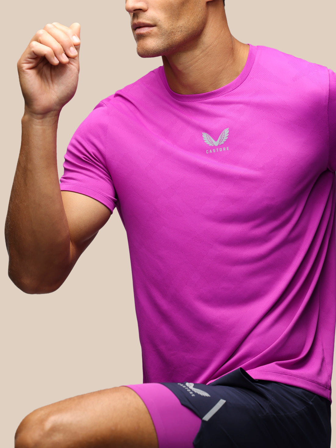 A man wearing a bright pink athletic t-shirt with a small white wing logo and the brand name 'Castore' on the chest, paired with dark navy athletic shorts.