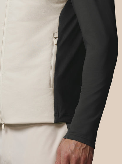Close-up of a person wearing a beige jacket with a black sleeve against a neutral background