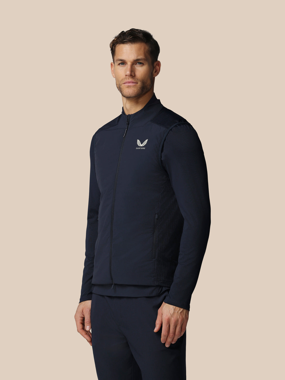 Man wearing a navy blue athletic jacket with a logo on a beige background
