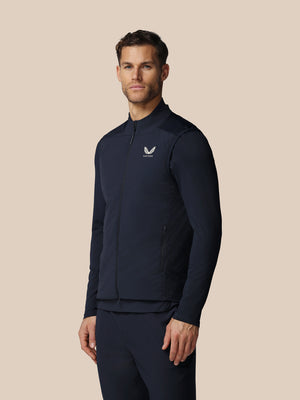 Man wearing a navy blue athletic jacket with a logo on a beige background