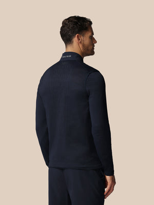 Man wearing a navy blue jacket with 'Castore' branding on the back against a beige background