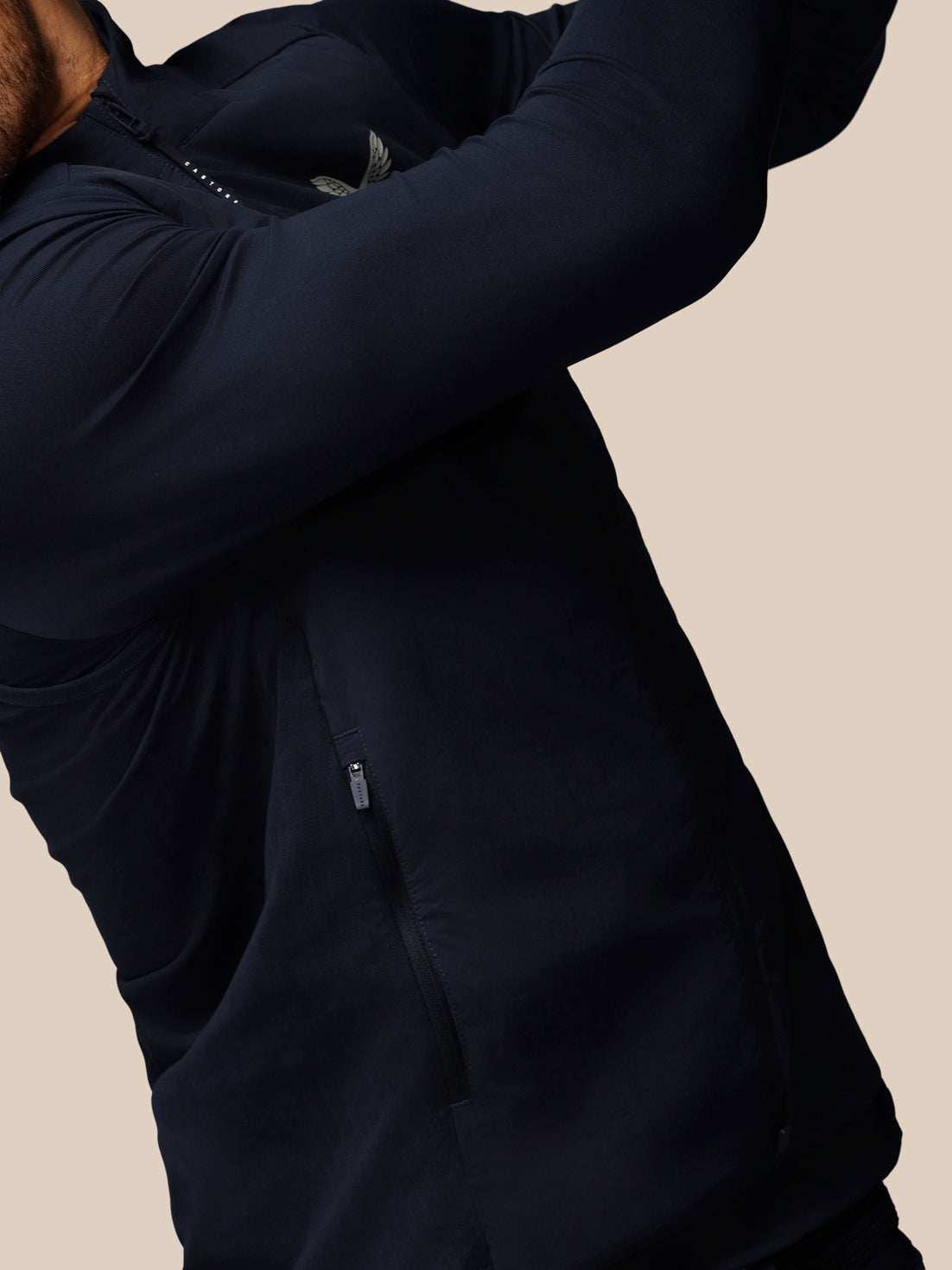 Person wearing a dark blue jacket with arms raised on a beige background